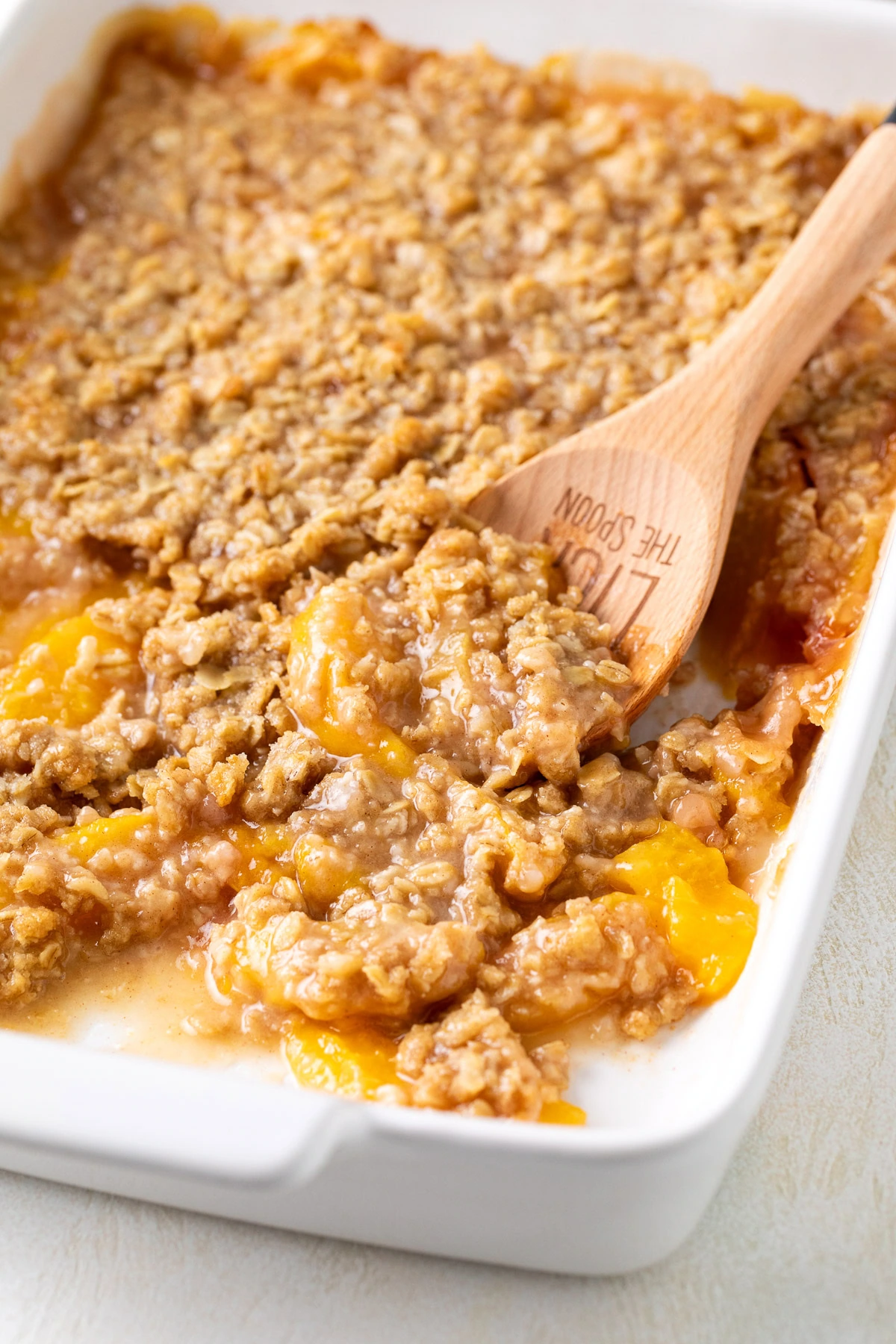 A wooden spoon scooping peach crisp from the pan.