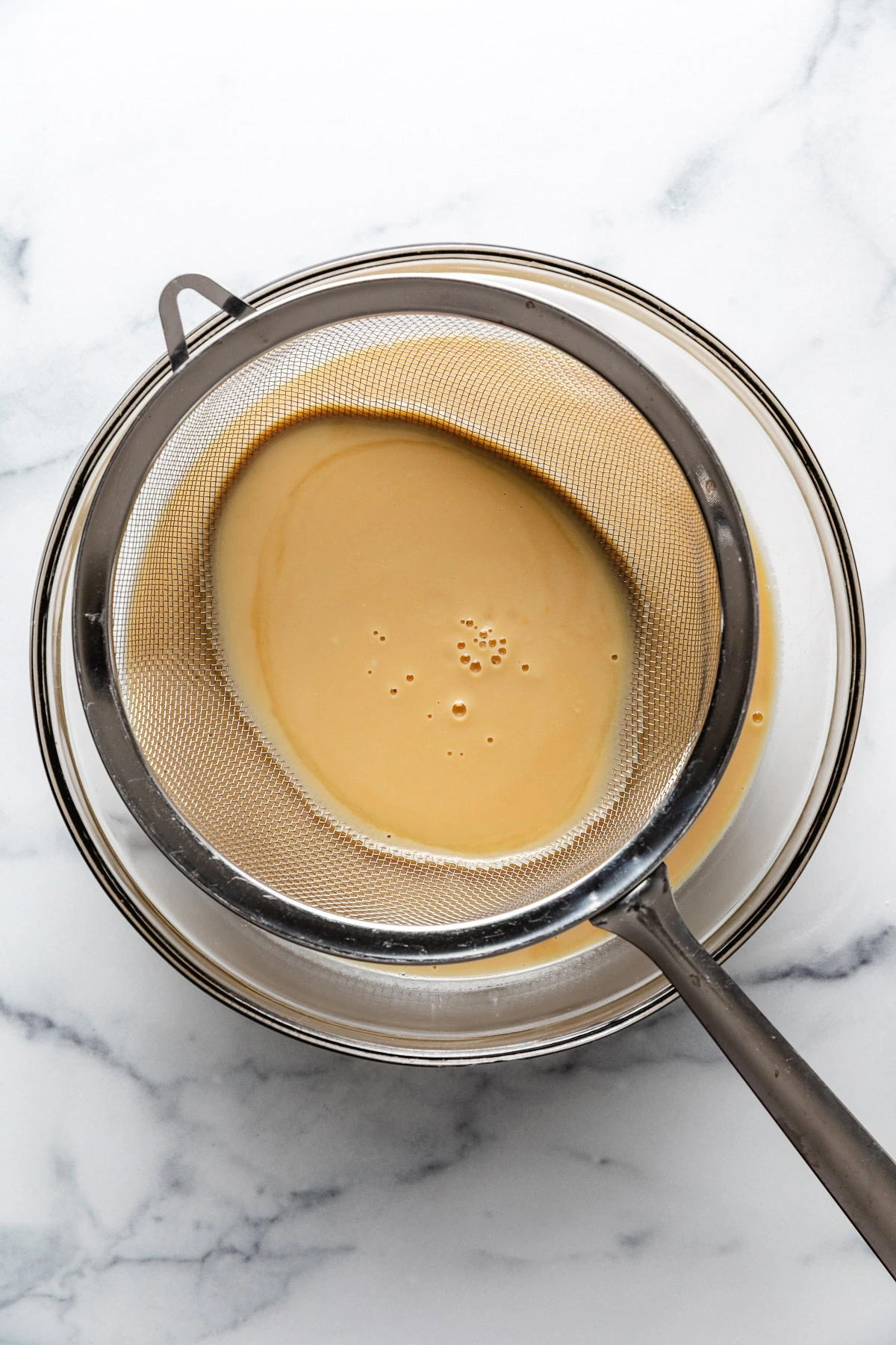 Ice cream custard being strained into a glass bowl.