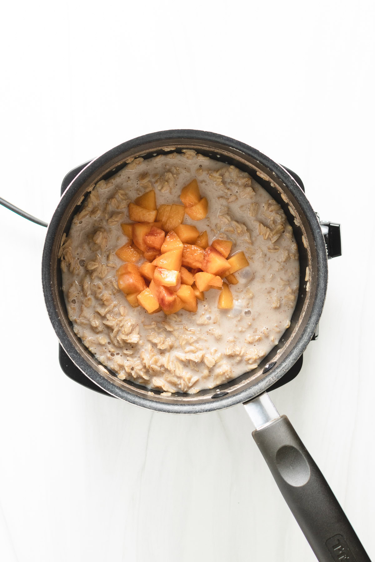 Fresh peaches added to a pan of oatmeal.
