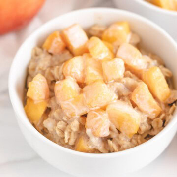 Close up view of a bowl of peaches and cream oatmeal in a white bowl.