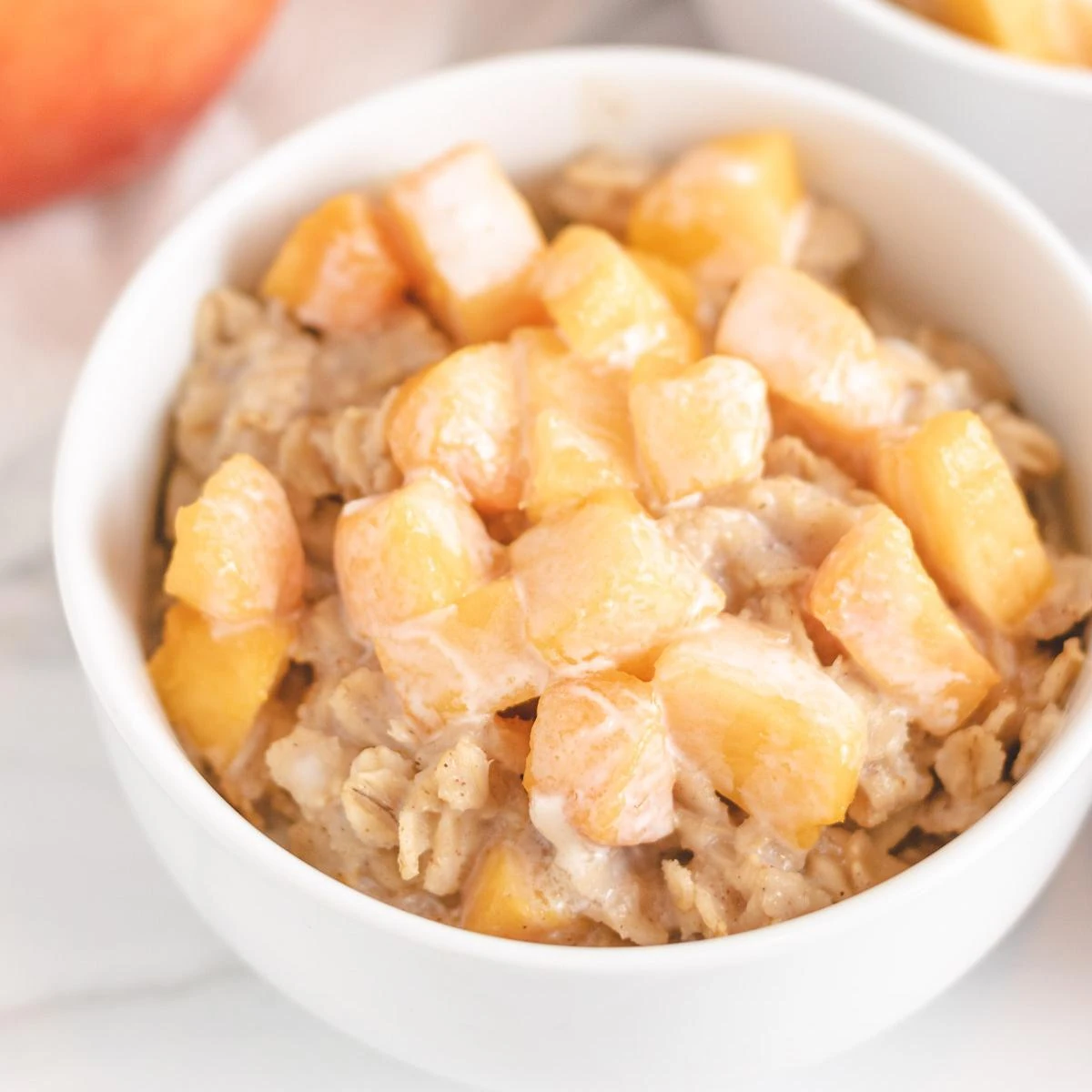 Close up view of a bowl of peaches and cream oatmeal in a white bowl.