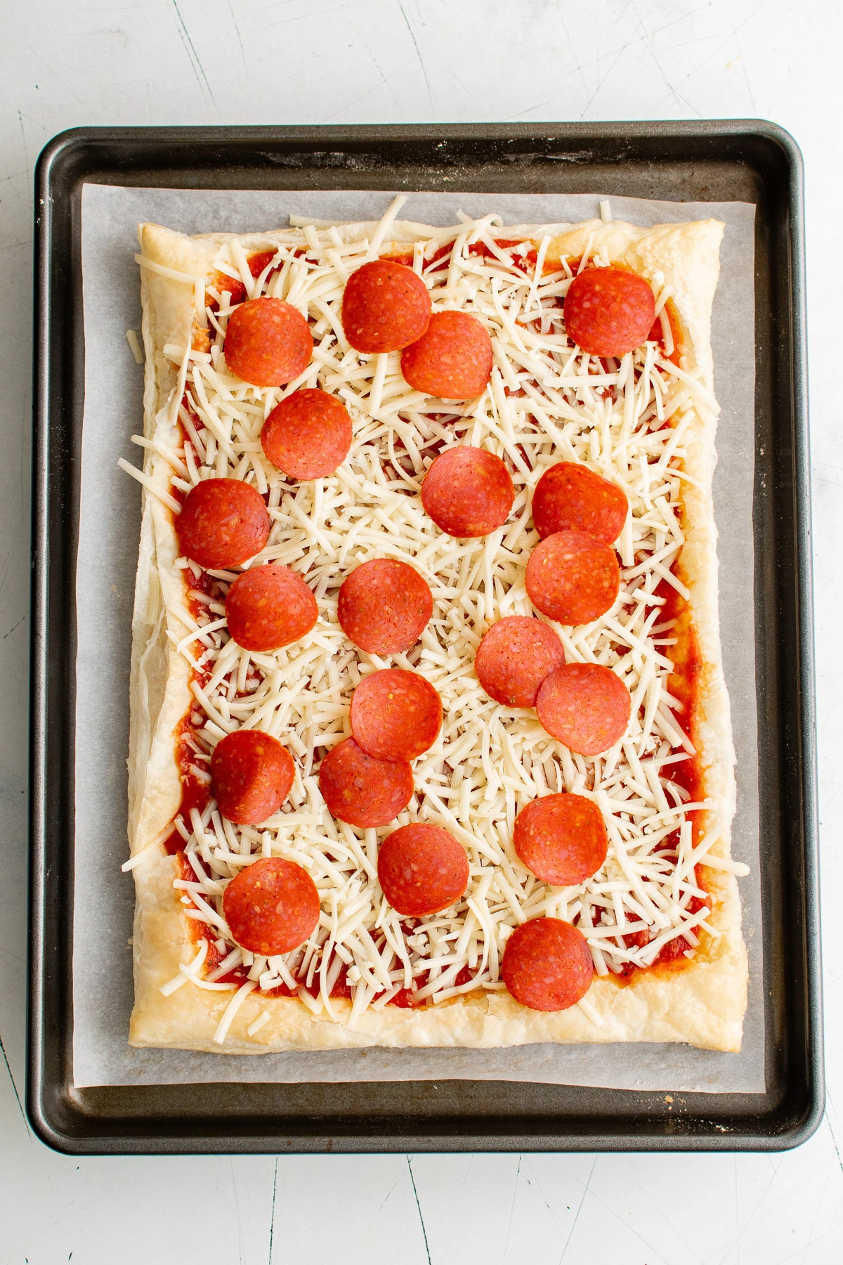 Pepperoni added to a sheet of puff pastry with cheese and sauce.