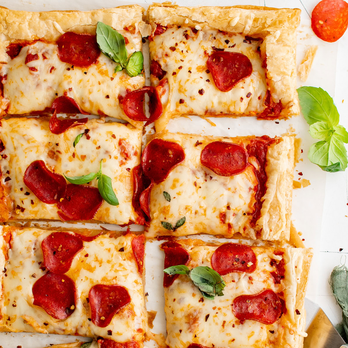 Overhead view of sliced puff pastry pizza topped with pepperoni and cheese.