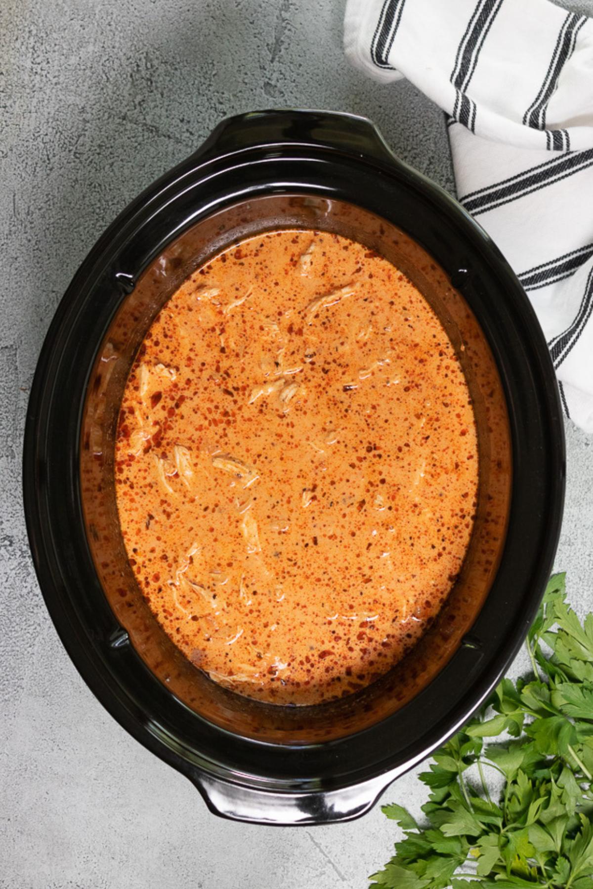 Creamy chicken pasta in a black slow cooker with herbs and spices.