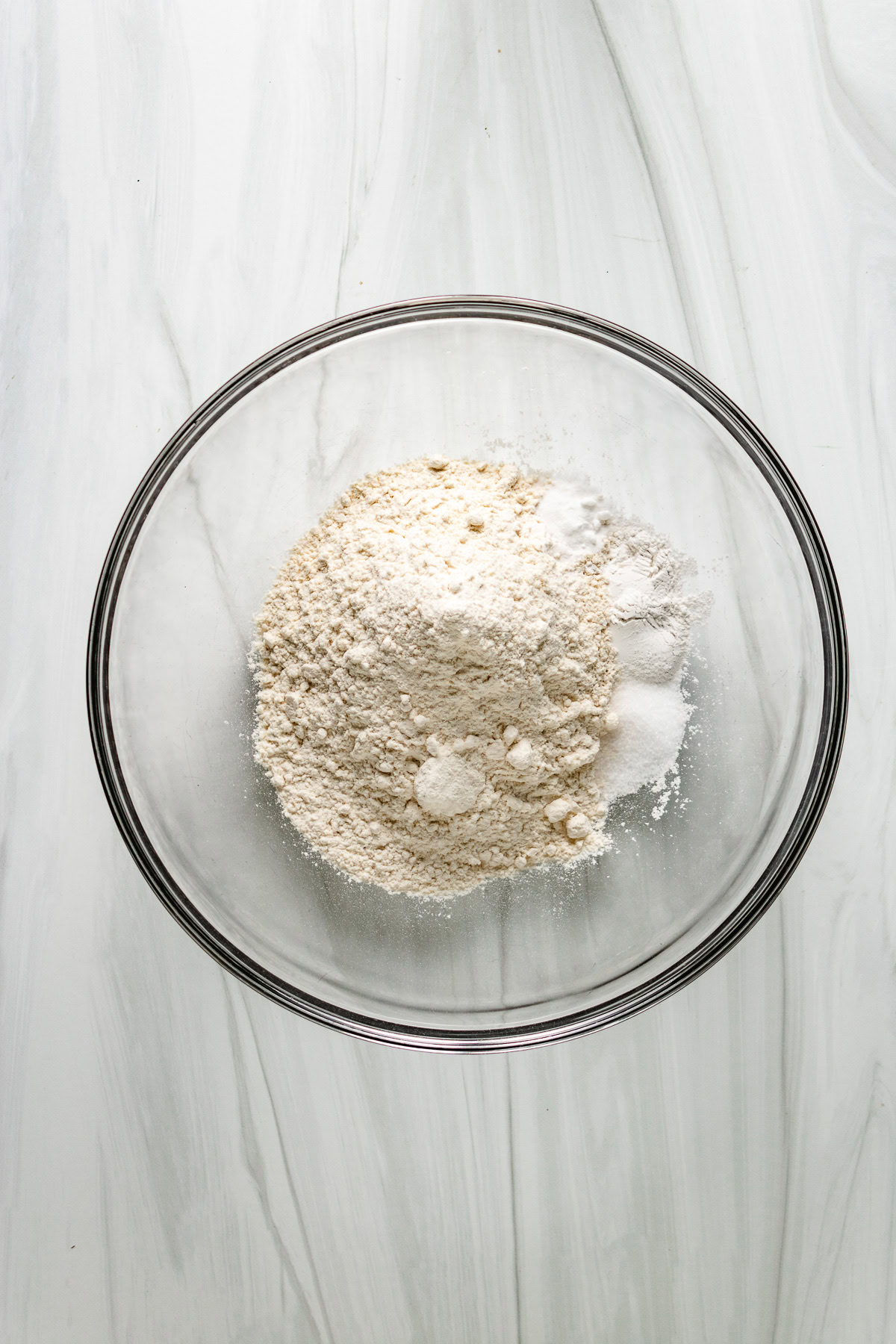 Flour and baking ingredients for sourdough biscuits in glass bowl.