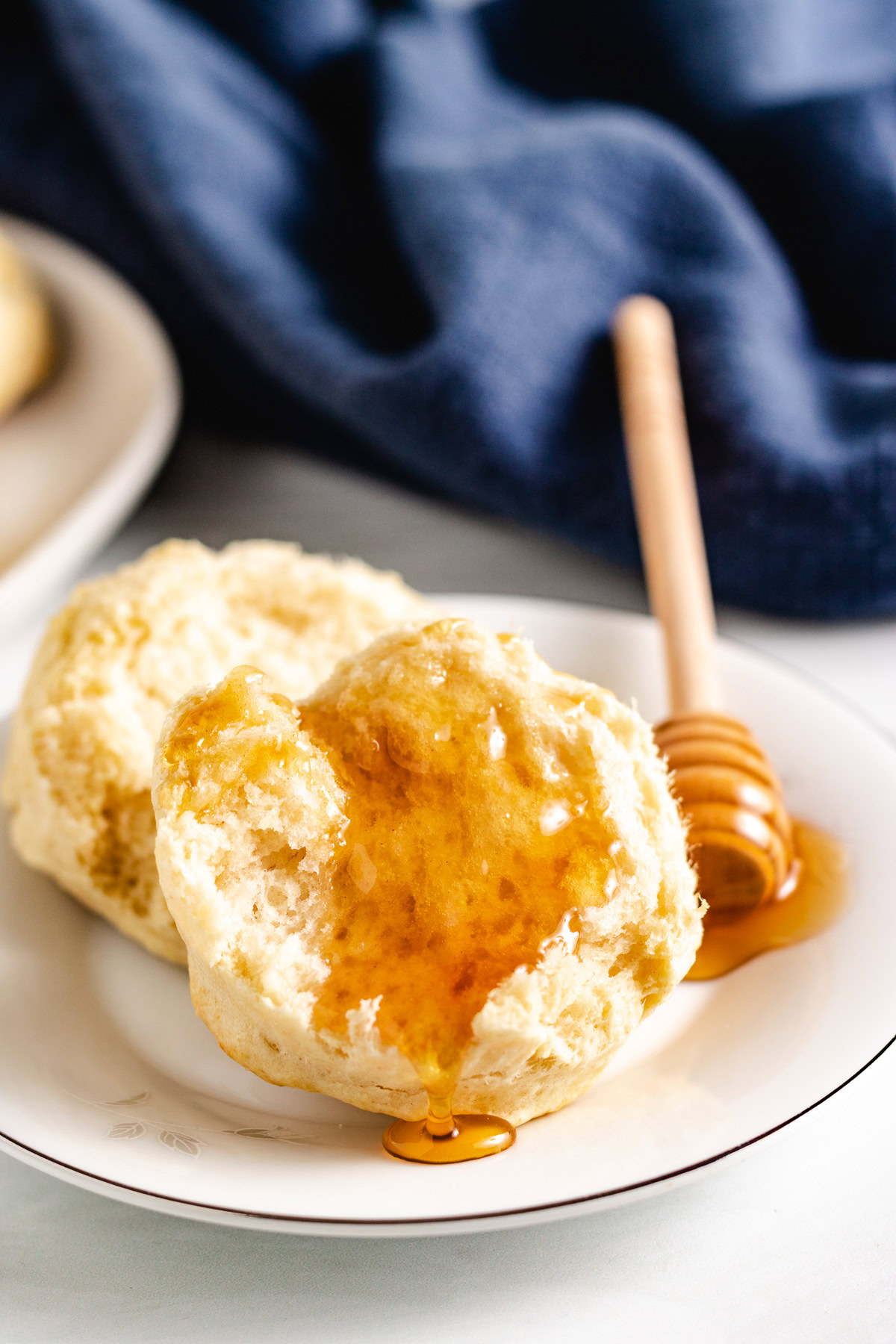 Fresh sourdough biscuit with honey drizzled on top on a white plate.