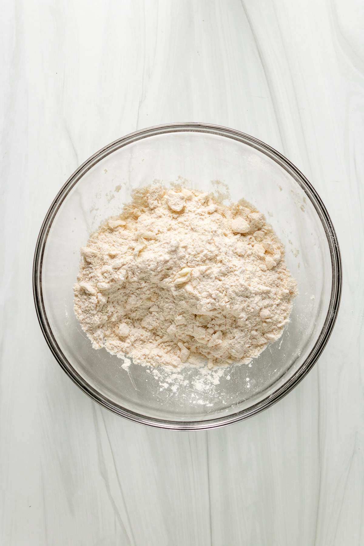 Flour mixture for sourdough biscuits in a glass bowl on white surface.