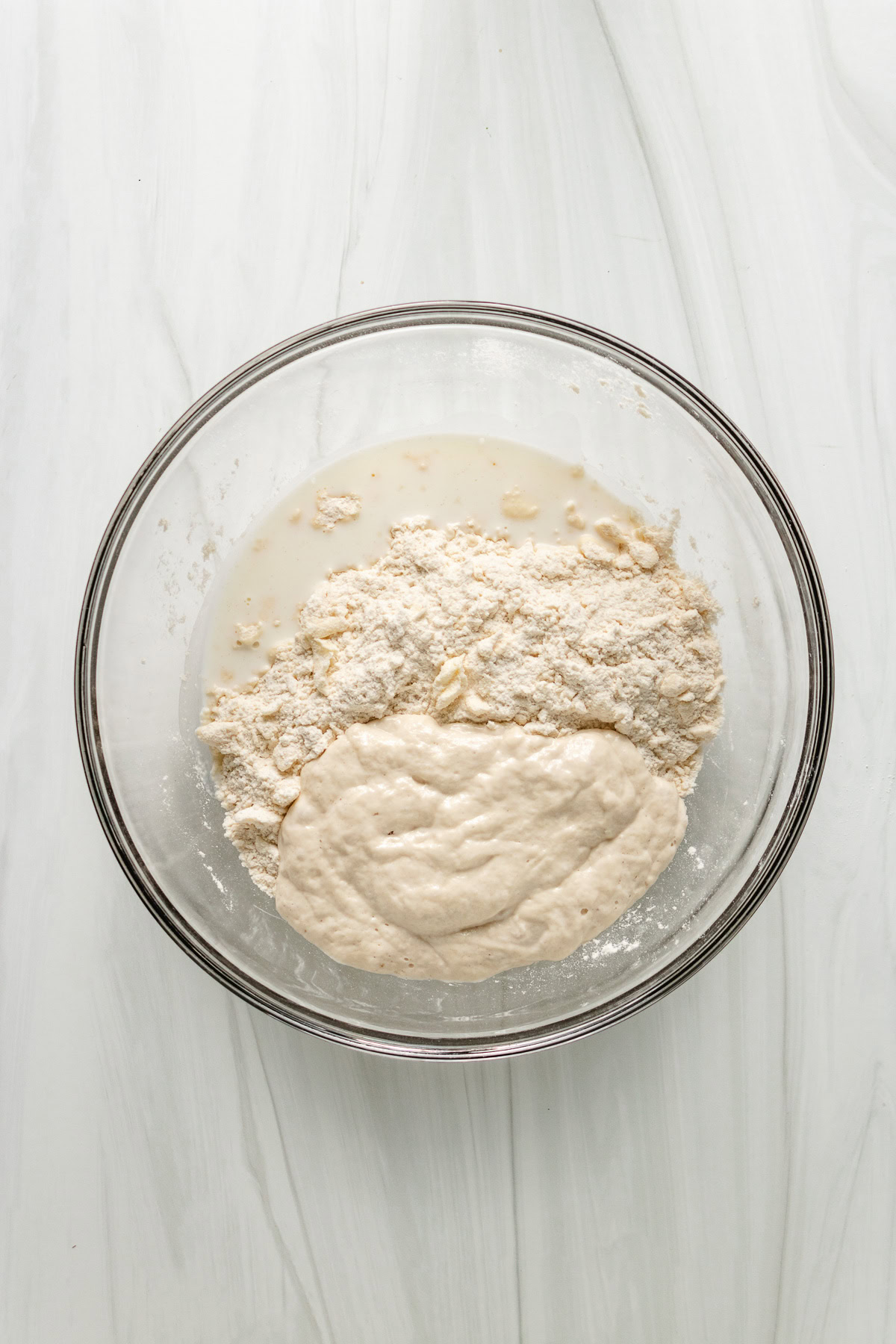 Mixing sourdough biscuit dough with flour, discard, and water in a glass bowl.