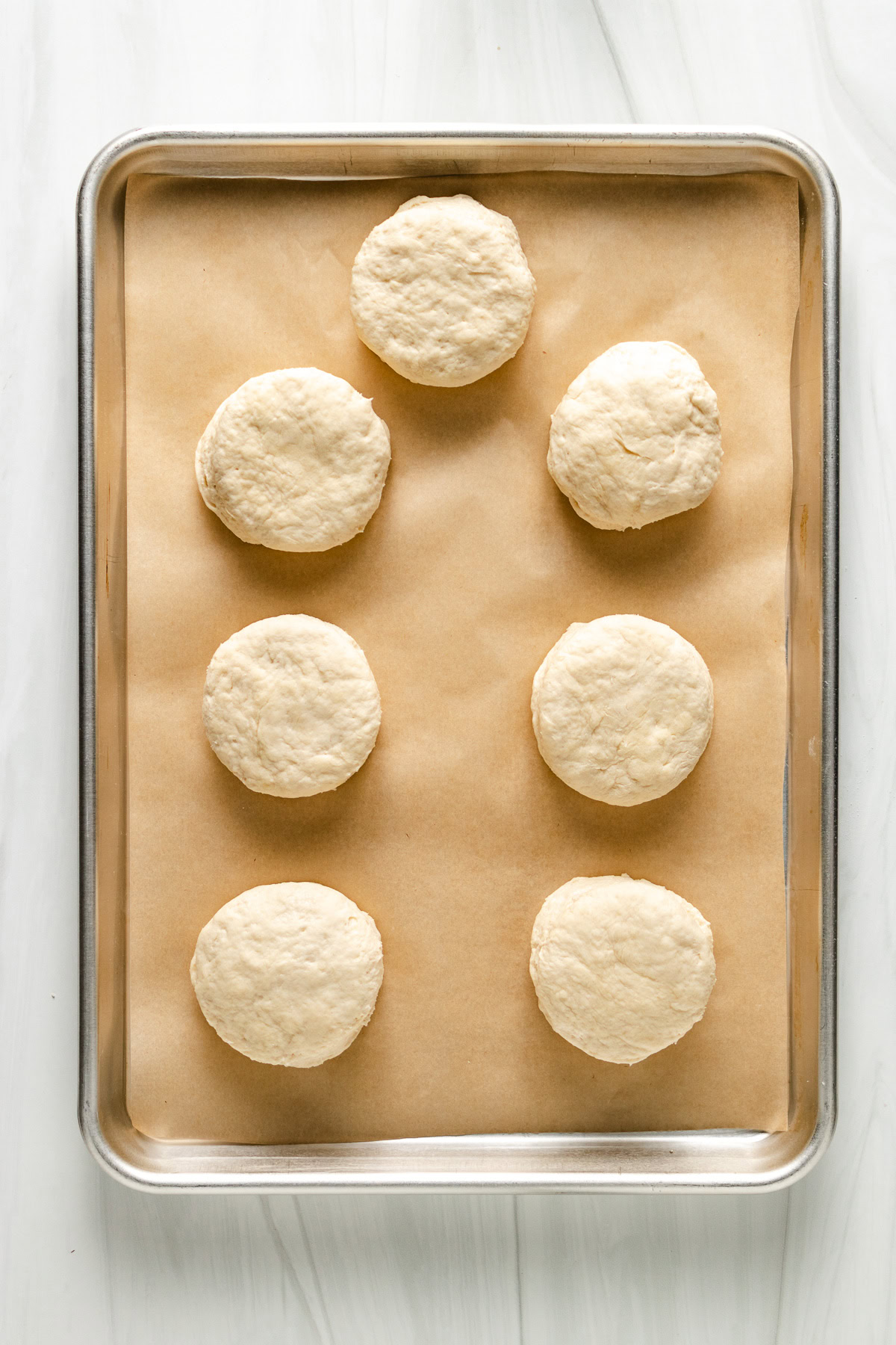 Raw sourdough biscuit dough balls on a baking sheet.
