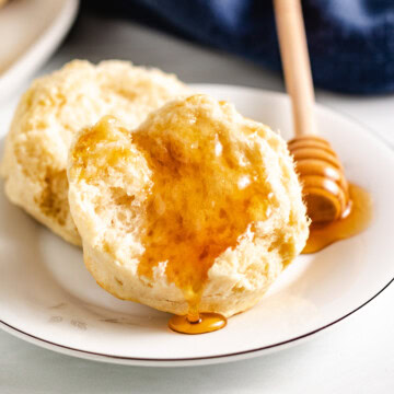 Fresh sourdough biscuits drizzled with honey on a white plate.