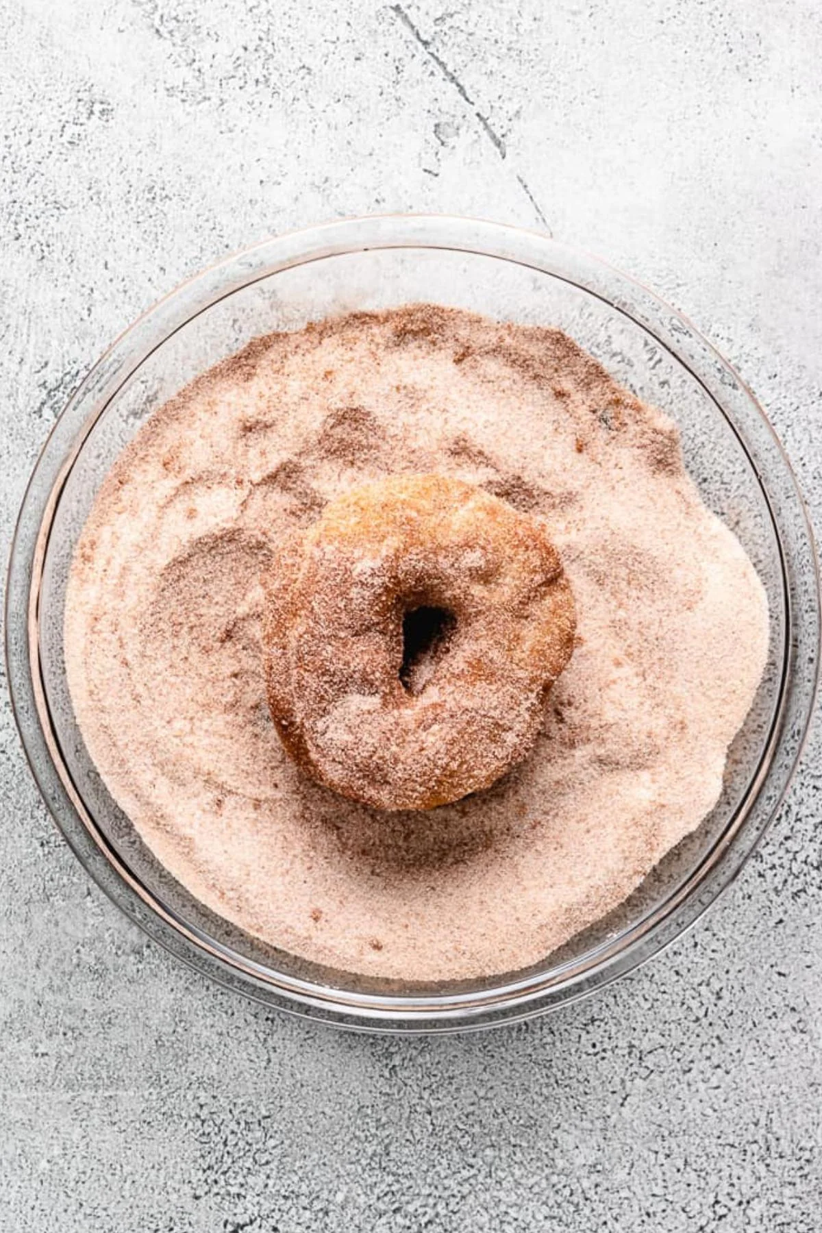 Freshly made doughnut being dipped into cinnamon and sugar.