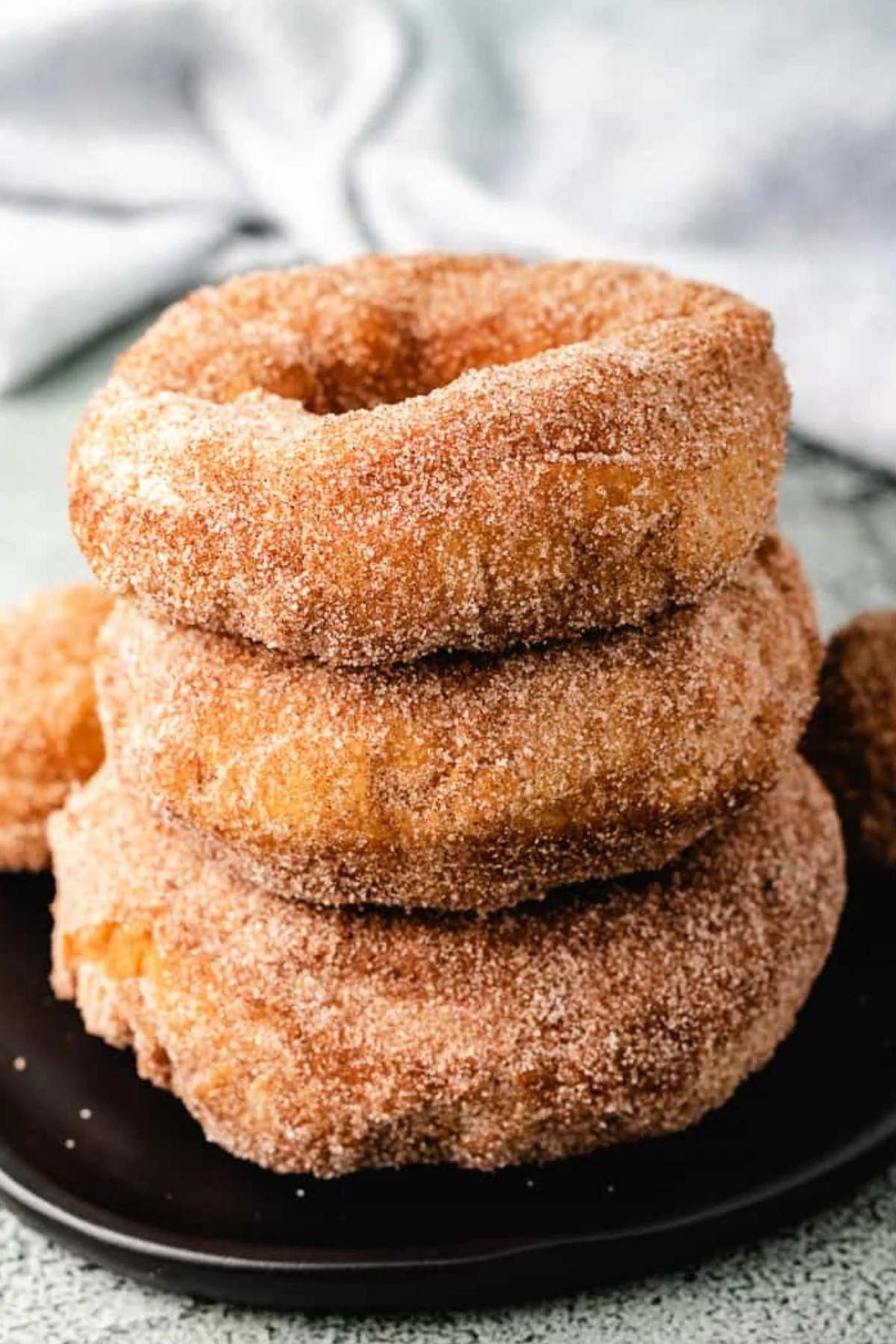 Stack of cinnamon sugar sourdough doughnuts on a black plate.
