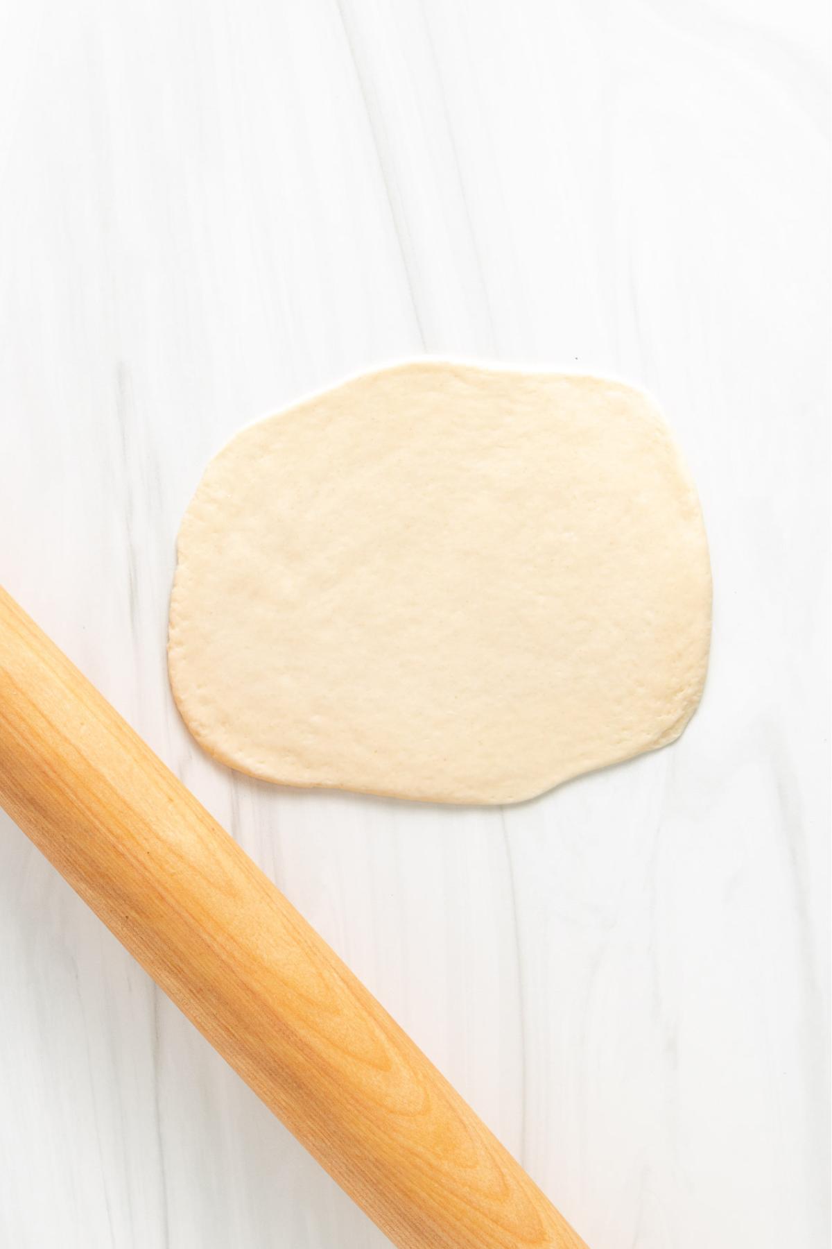 Naan dough rolled out into a flat circle.