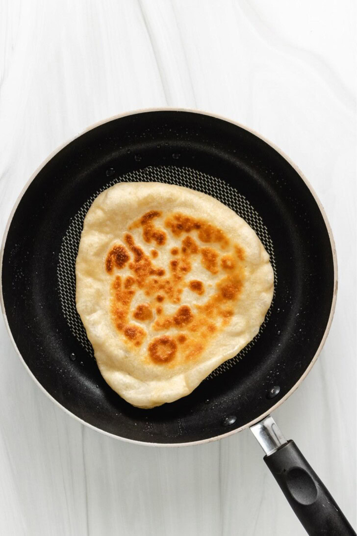 Naan bread cooking in a skillet.