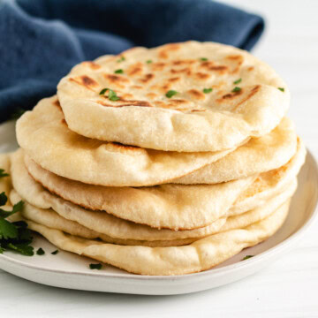 Close up view of sourdough naan bread stacked on a plate.