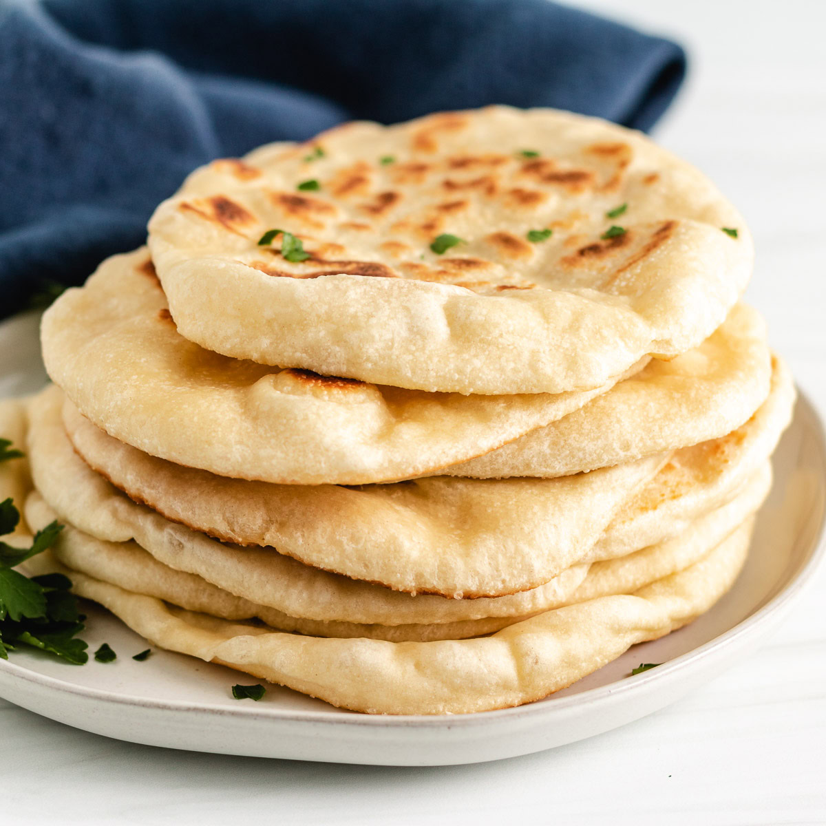 Close up view of sourdough naan bread stacked on a plate.