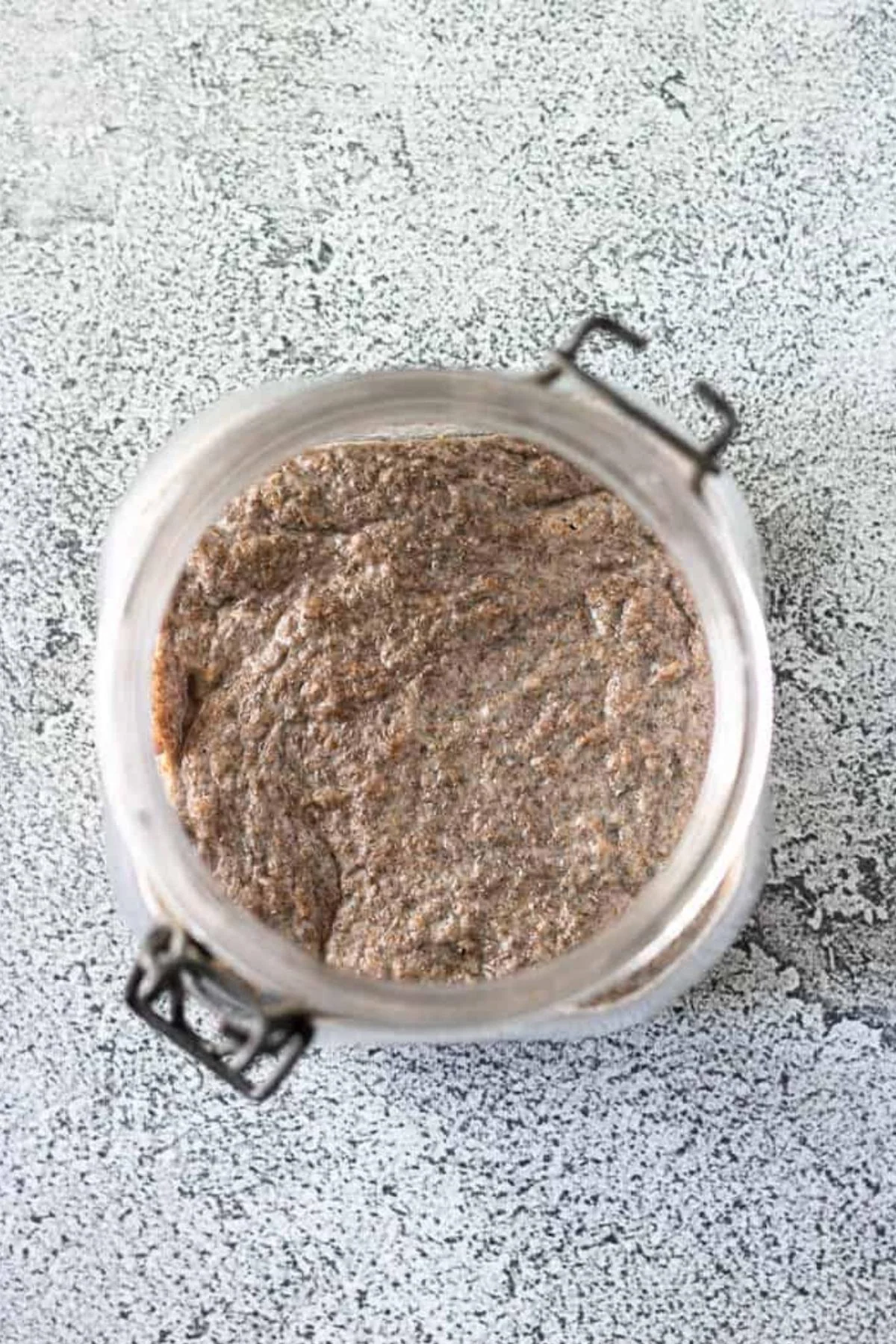 Thick whole wheat sourdough starter mixture in a glass jar.