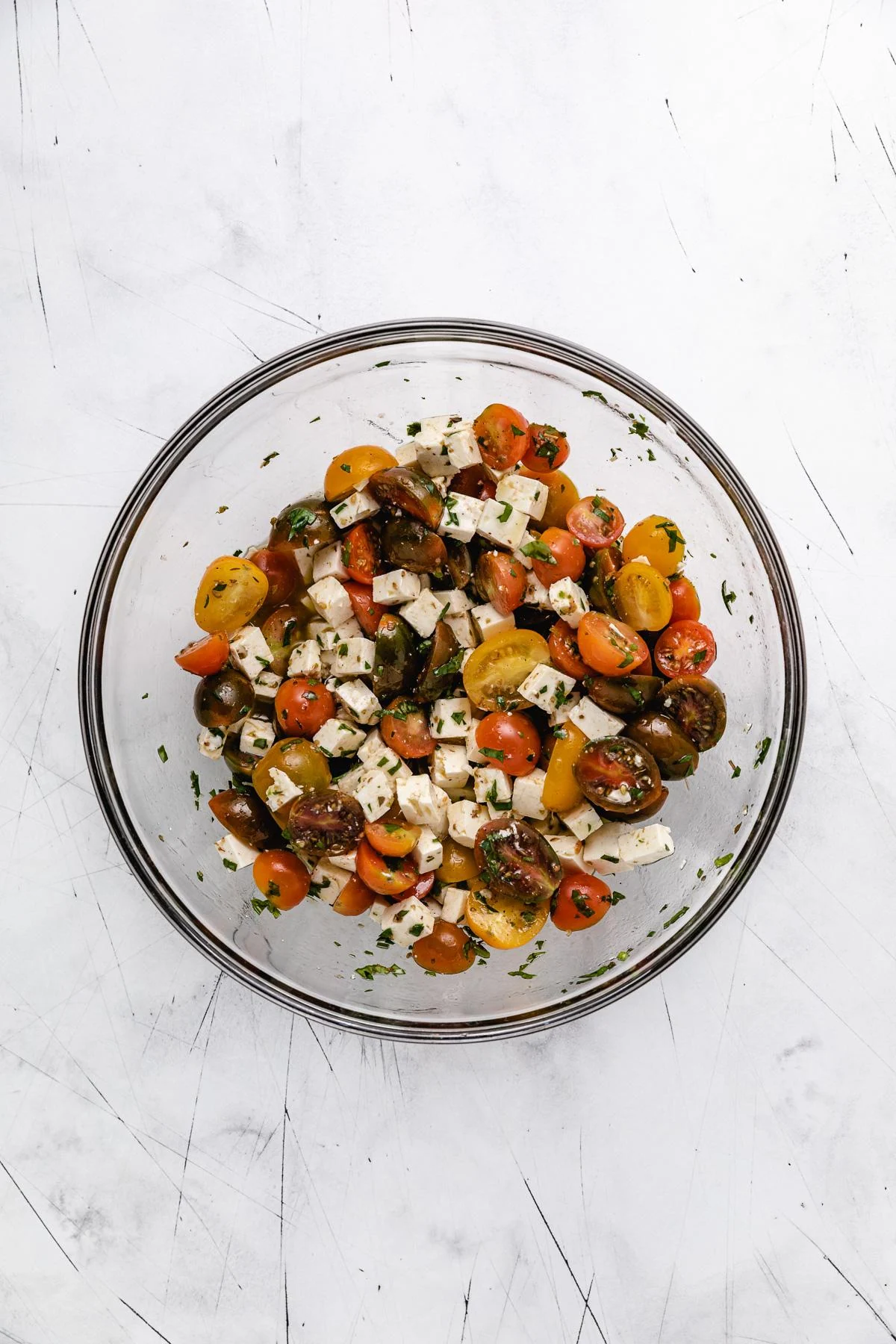 Ingredients for tomato and feta salad tossed together in a glass mixing bowl.