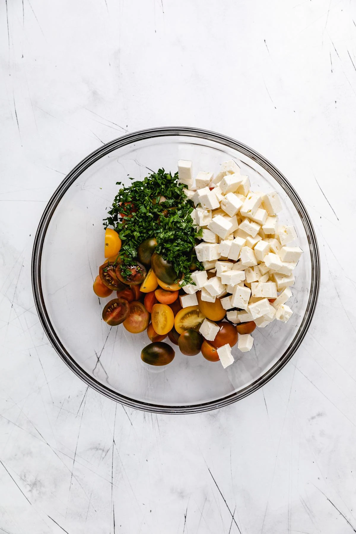 Ingredients for tomato feta salad in a glass mixing bowl.