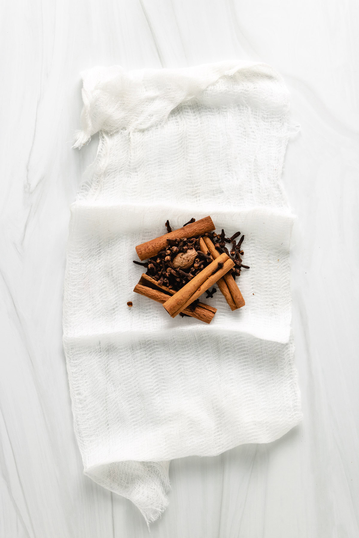 Whole spices arranged on a piece of cheesecloth.