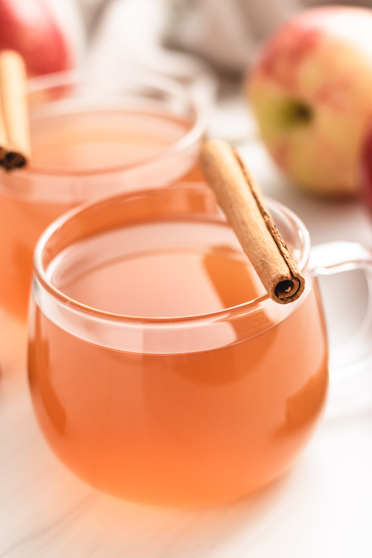 Two glasses of spiced apple cider with fresh apples.