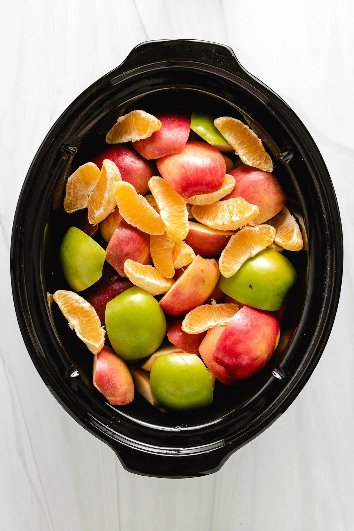 Chopped apples and orange slices in a slow cooker.