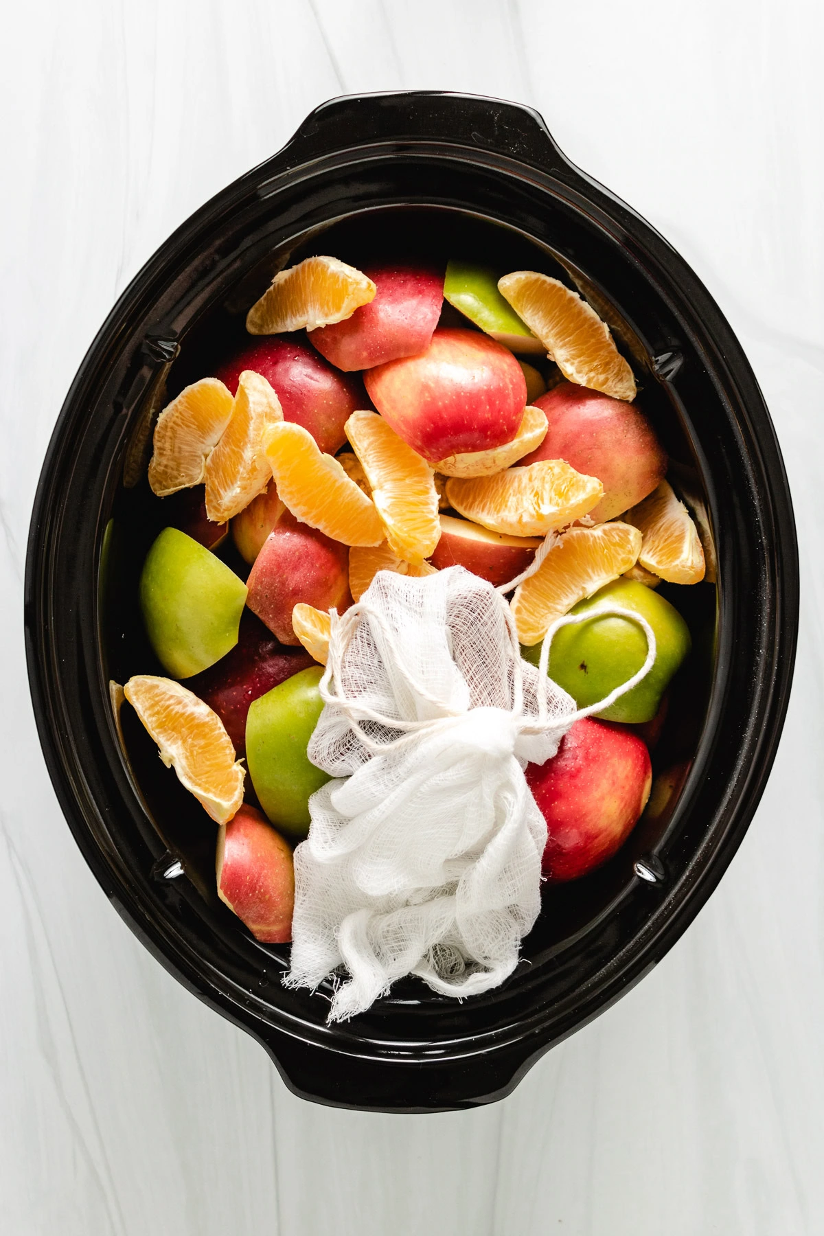 Apples, oranges, and a spice bundle in the slow cooker.