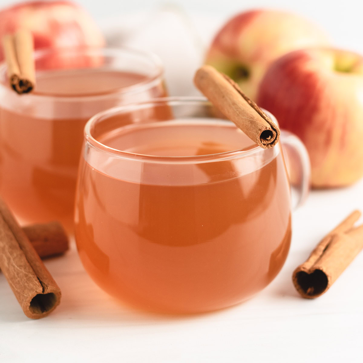 Warm apple cider in glass mugs with cinnamon sticks.
