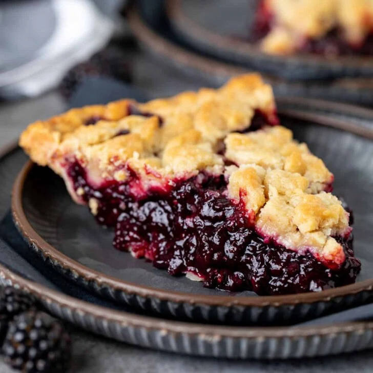 Slice of blackberry crumble pie on a dark plate.
