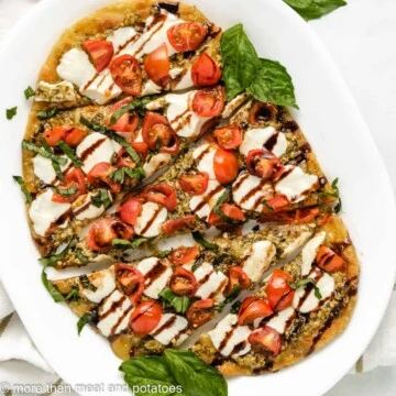 Overhead view of caprese flatbread on a white plate.