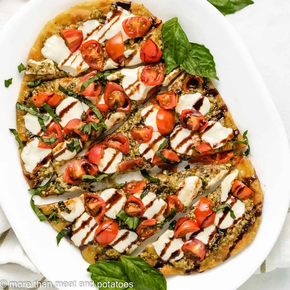 Overhead view of caprese flatbread on a white plate.