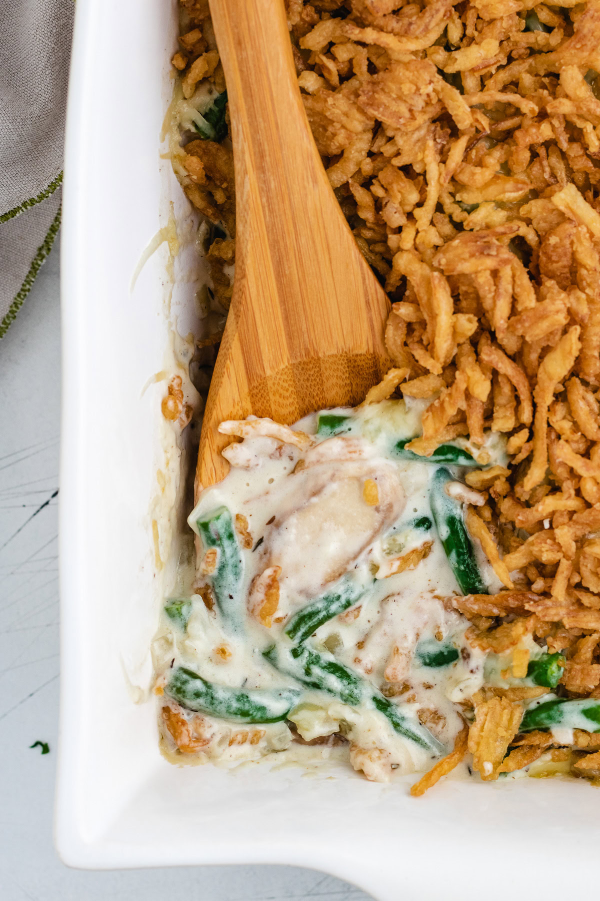 Green bean casserole being served with a wooden spoon.