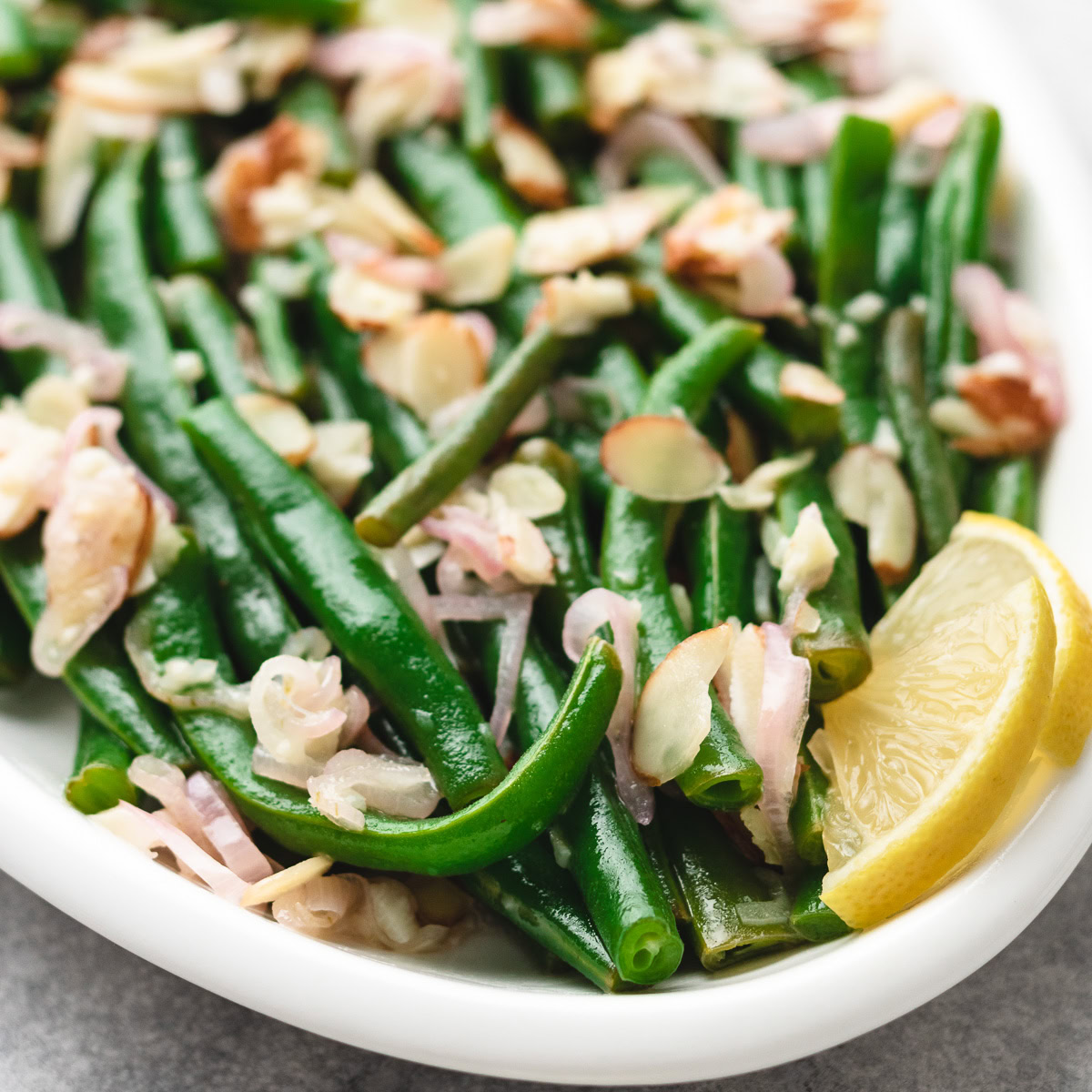 Fresh green beans with sliced almonds and lemon wedge in a white bowl.