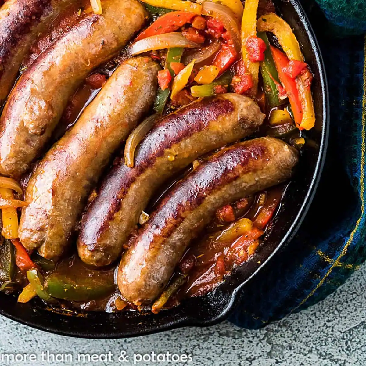 Four browned sausages in a skillet with sautéed bell peppers, onions, and tomato sauce.