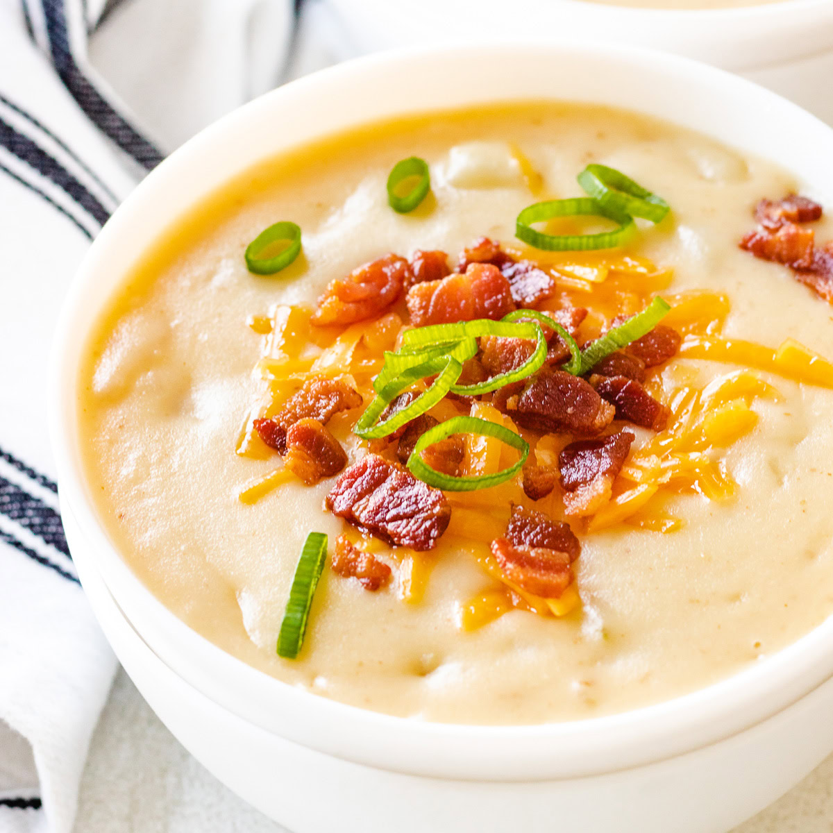 Green onions, bacon, and cheese on a bowl of creamy soup.