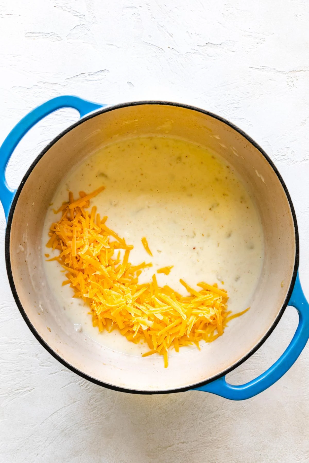 Shredded cheddar cheese added to a pan of potato soup.