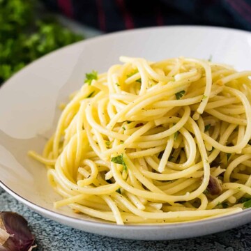 A white bowl filled with spaghetti tossed with oil, herbs, and garlic.
