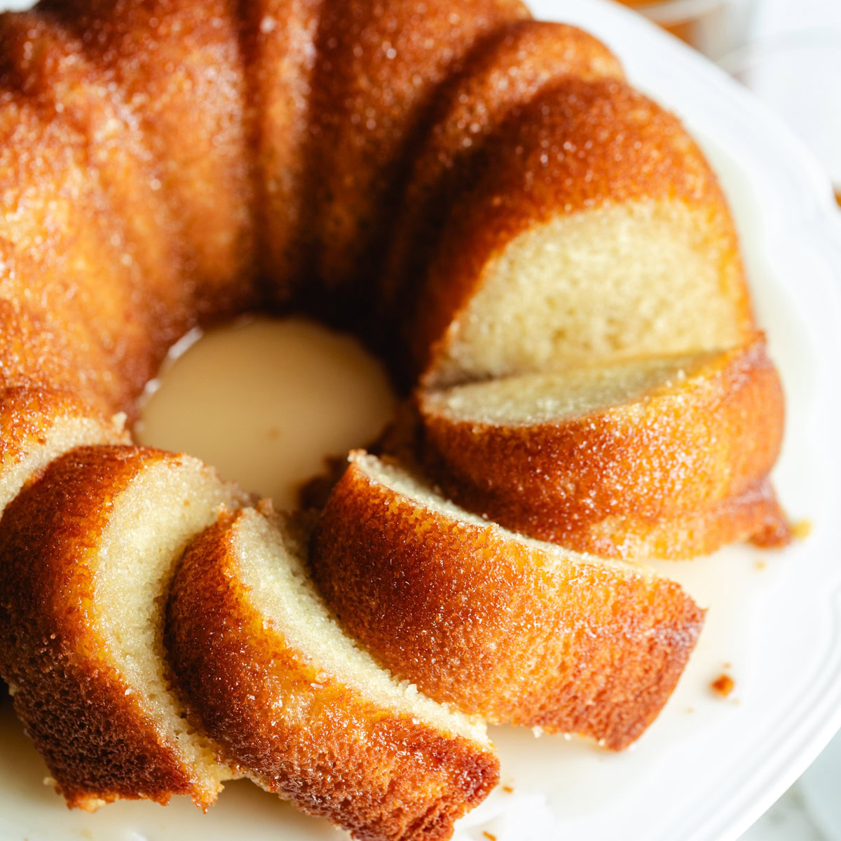 Overhead view of a sliced rum cake on a white platter.