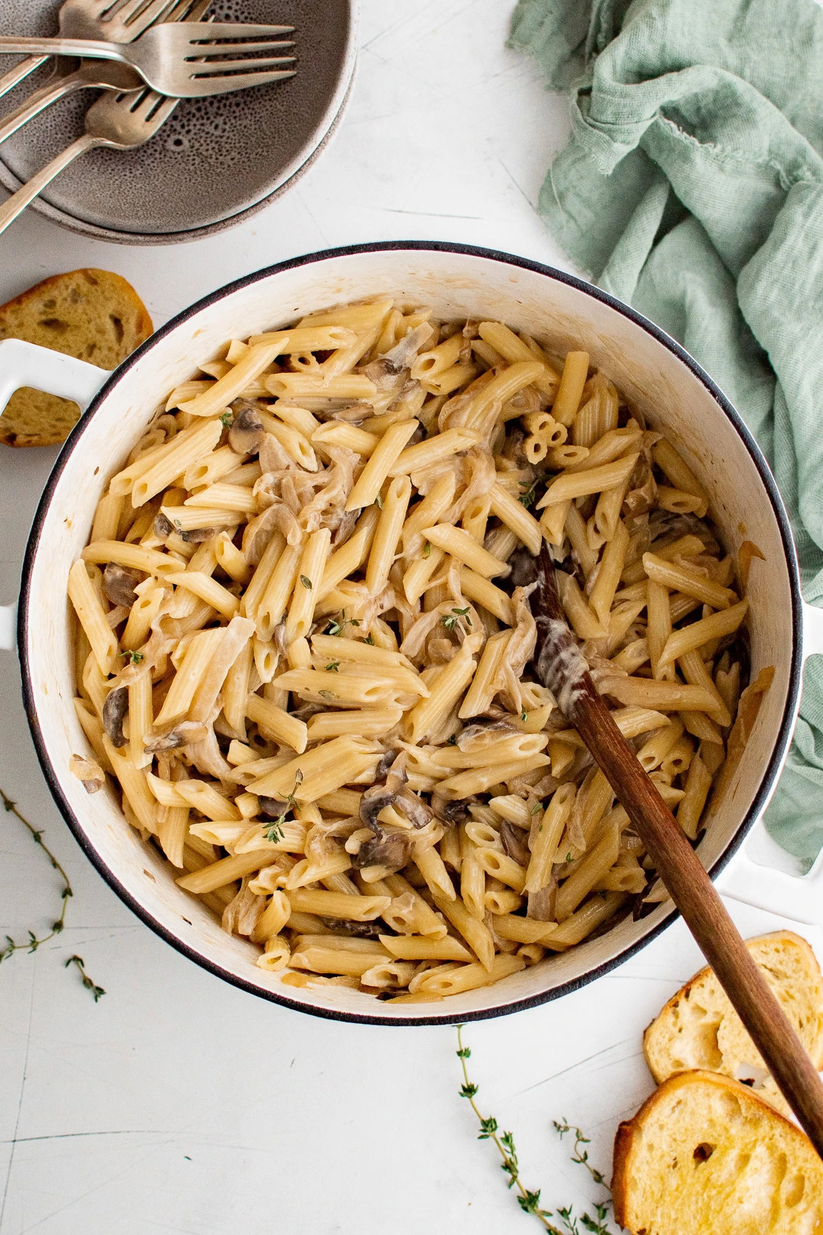 Overhead view of a pot of French onion pasta next to baguette slices.