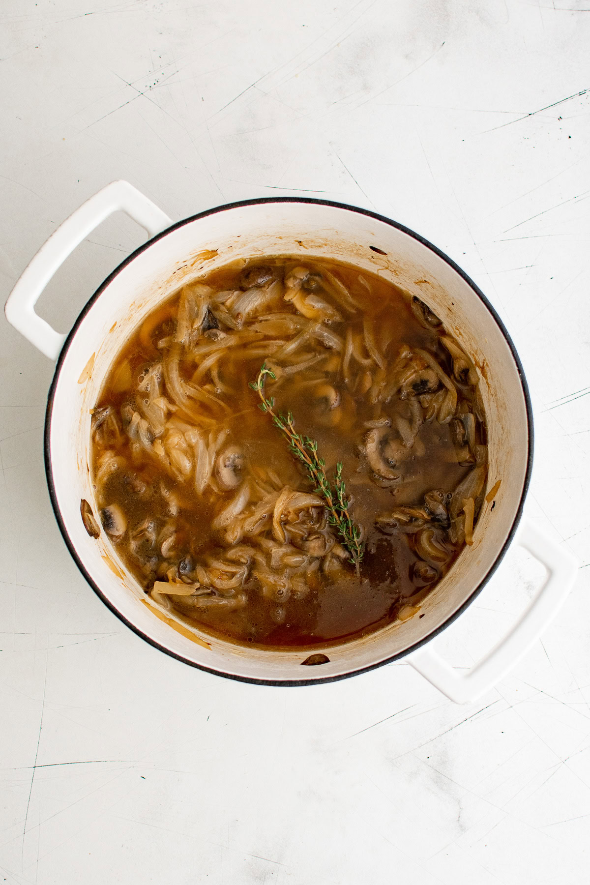 Beef broth and fresh thyme added to a pan of onions and mushrooms.