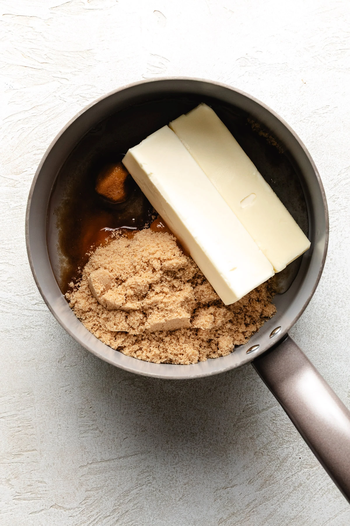 Two sticks of butter and a mound of brown sugar inside a saucepan.